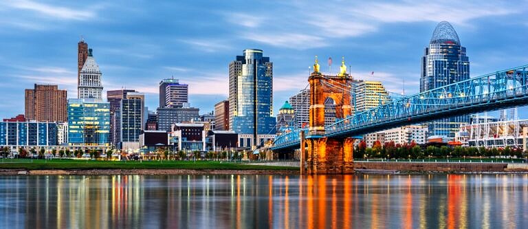 The suspension bridge across the Ohio river lit up at dusk and leading into the city of Cincinnati on a cloudy evening.