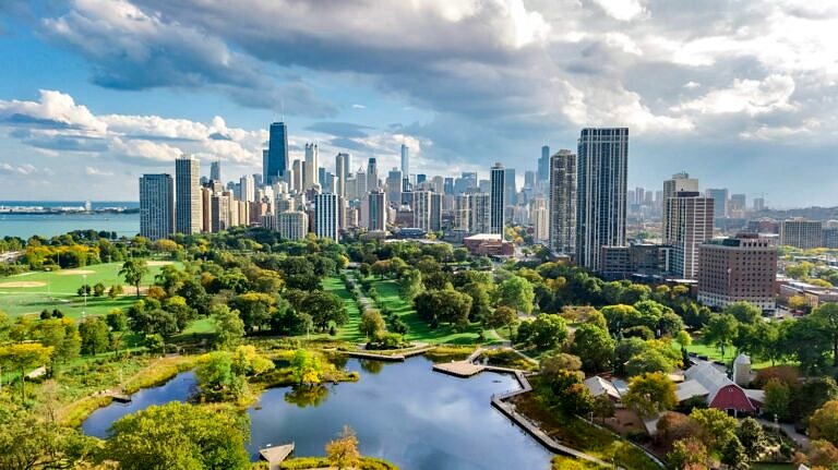 The skyline of Chicago, IL on a bright, partly cloudy day with a park and small lake in the foreground.