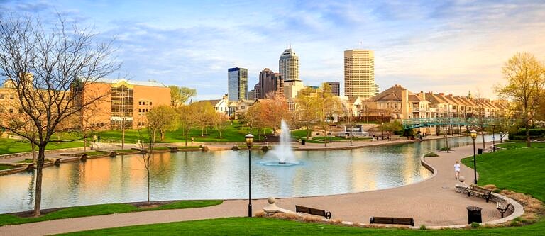 The Indianapolis skyline as seen from across a water feature at a park on a warm autumn day.