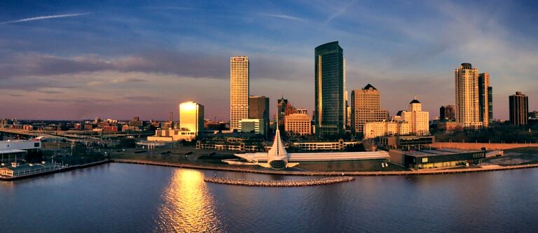 The Milwaukee, WI skyline from across the water at sunset with a partly cloudy sky.