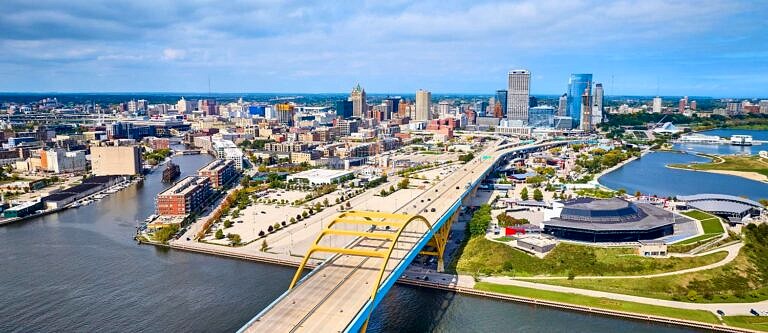 Milwaukee, WI as seen from above and across an arched bridge over the nearby river on a bright sunny day.