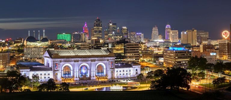 A view of KCMO from an elevated area at night with bright lights shining from the buildings.