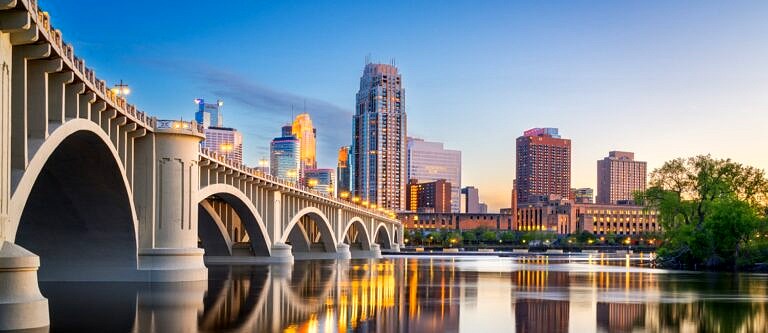 Minneapolis as seen from across the water with the bridge in the frame as the sun sets.