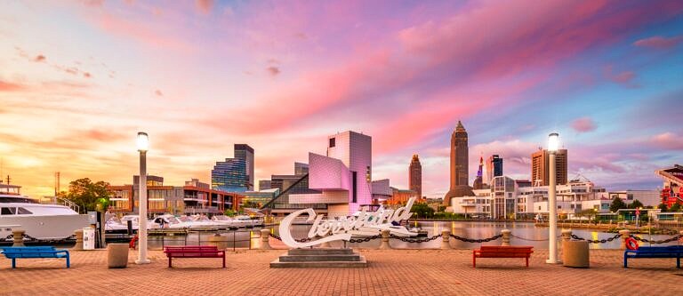 The "Cleveland" sign with a wide shot of the city skyline in the background at sunset. There are some clouds in the sky accenting pink, purple, and orange.