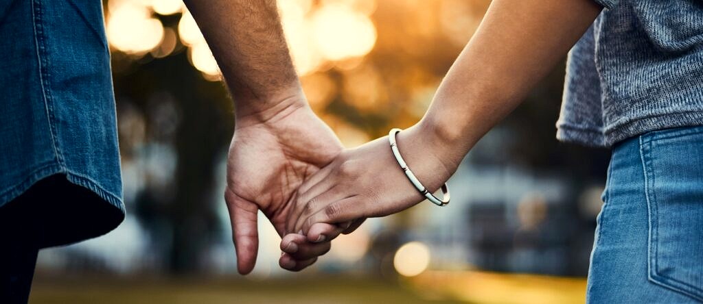 A close up image of a couple holding hands as they walk outside together.